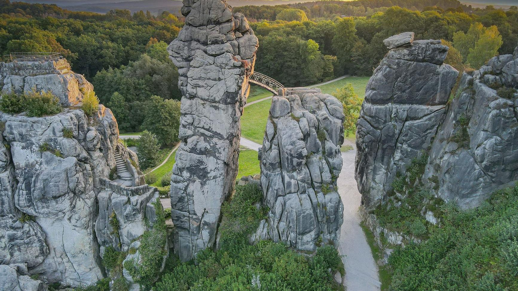 gray rock formations on green grass field near the forest